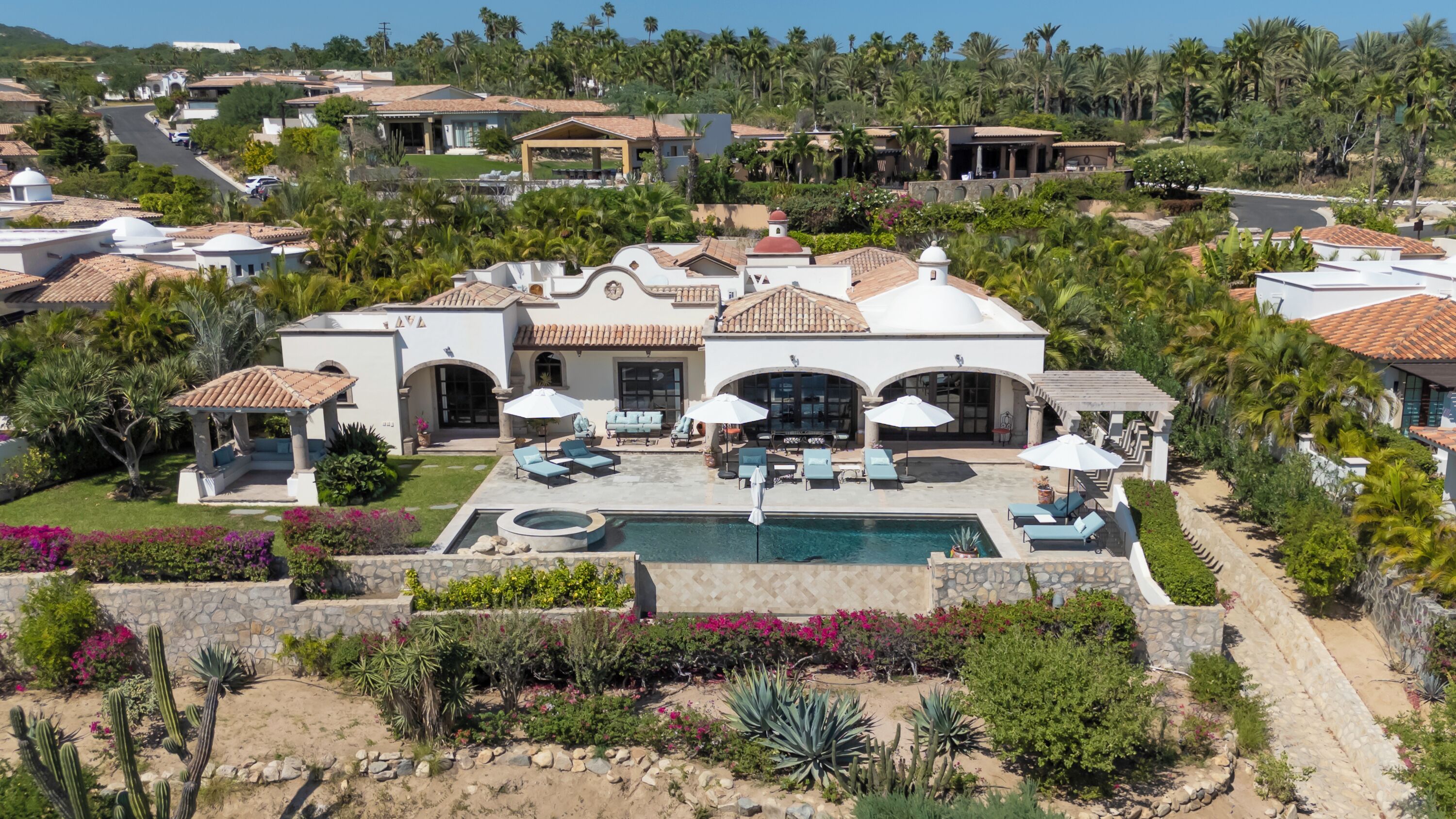Una casa grande con piscina, varias zonas de estar al aire libre y un exuberante paisaje.
