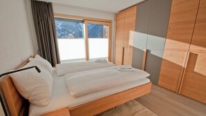 A modern bedroom with a large bed, wooden wardrobe, and a view of a snowy landscape. - Apartment Jua (Zermatt)