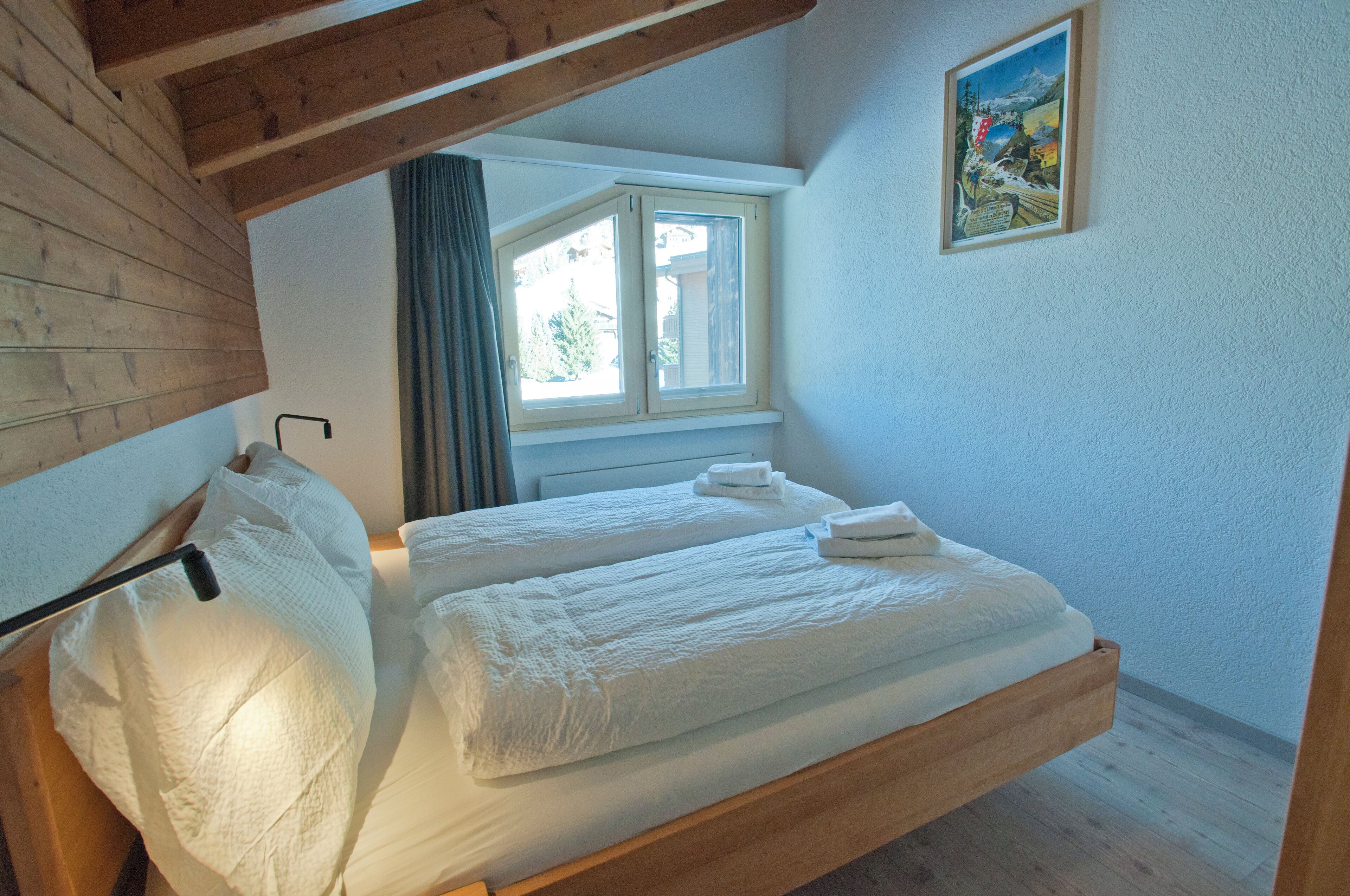 A bedroom with two beds, wooden beams, a window with curtains, and a painting on the wall.