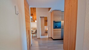 A narrow hallway with wooden flooring and walls, leading to a kitchen area with wooden cabinets and a blue countertop. - Apartment Jua (Zermatt)