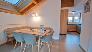 A dining area with a wooden table and chairs, a skylight, and a view of the kitchen. - Apartment Jua (Zermatt)