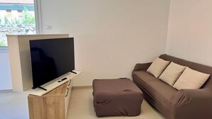A modern living room with a flat-screen TV on a wooden stand, a brown sofa with cushions, and a small ottoman. - Domus Aurus Family, Domus Aurus Family  (Bardolino)