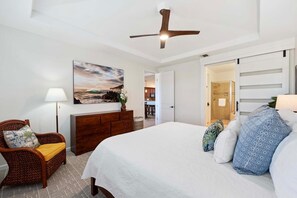 Ein Schlafzimmer mit Bett, Sessel, Kommode, Deckenventilator und einem Bild an der Wand.