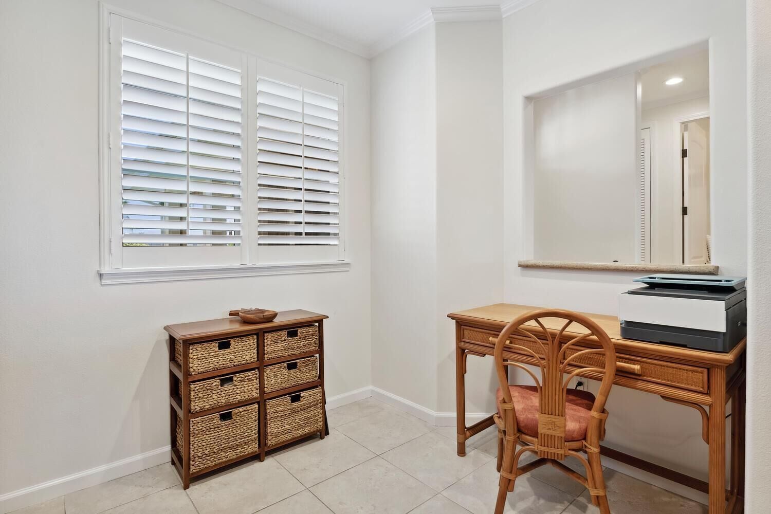A room with a desk, chair, wicker storage unit, and a window with blinds.