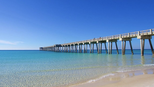 Un muelle se adentra en aguas azules y tranquilas bajo cielos despejados.