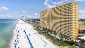 Un hotel de gran altura con vista a la playa, una extensa playa de arena y un muelle al fondo.