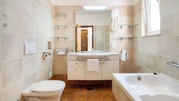 A bathroom with a toilet, sink, and bathtub. There are glass shelves above the sink and a mirror above the bathtub.