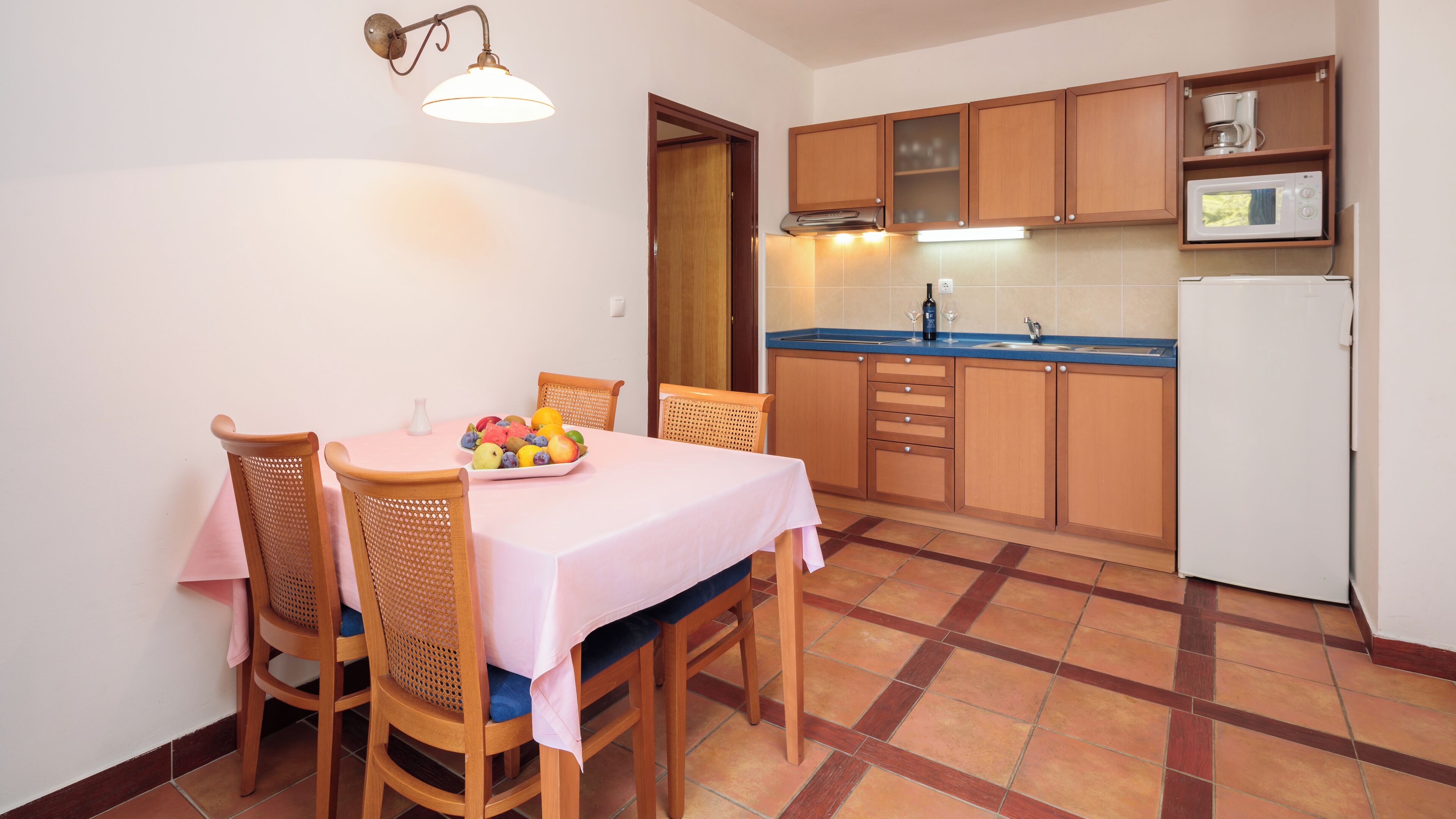 Cocina compacta con armarios de madera, microondas integrado y comedor con mesa para dos.