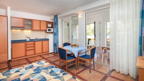 A compact kitchen with wooden cabinets, a microwave, and a coffee maker. There is a dining area with a table and chairs, and a patterned rug on the floor. - Fontana Bayside Park (Jelsa)