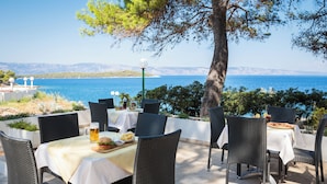 An outdoor dining area with tables and chairs, a view of the sea, and a lamp post. - Fontana Bayside Park (Jelsa)