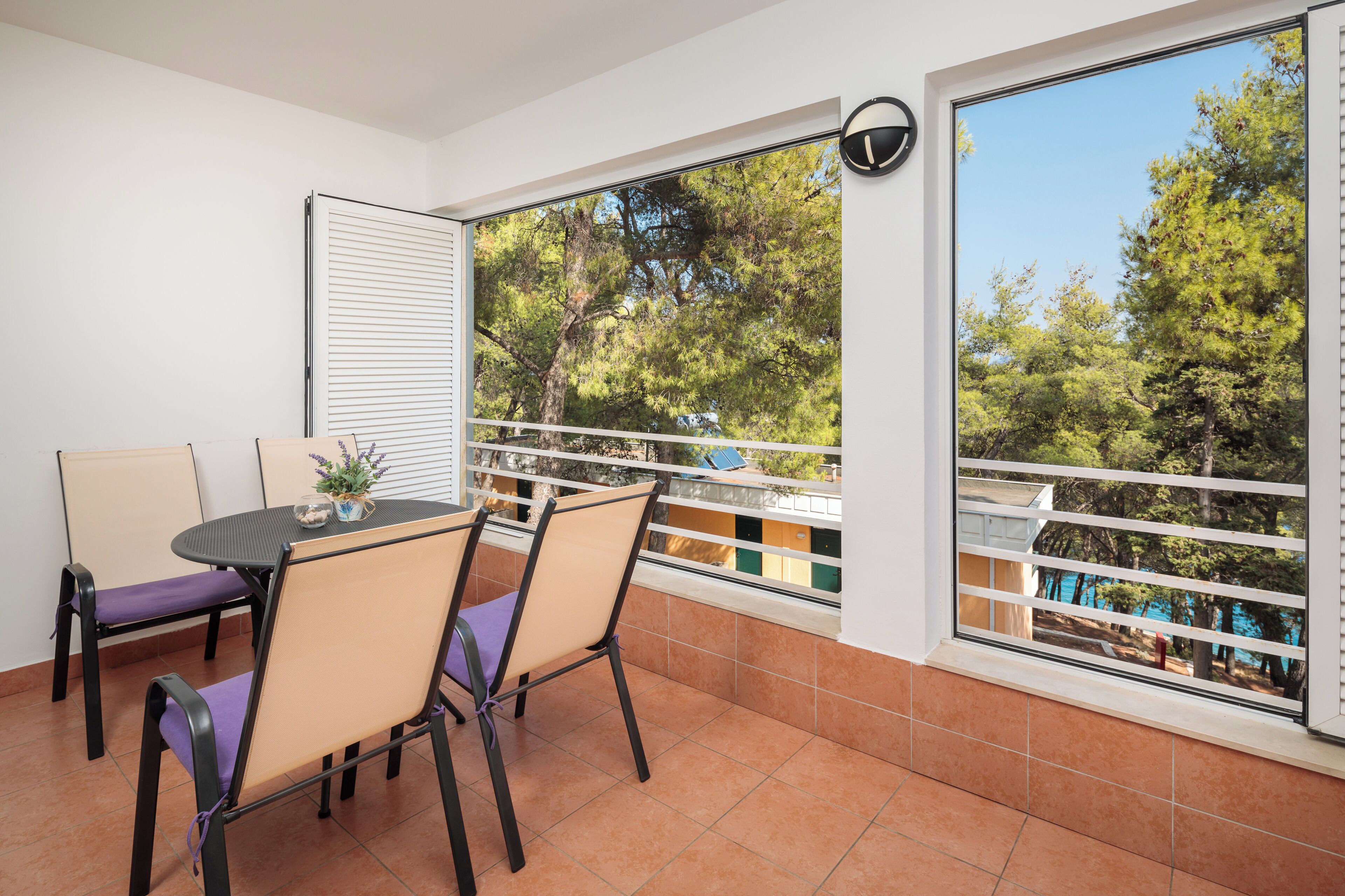 Un balcón con mesa y sillas, vistas a árboles y una piscina.