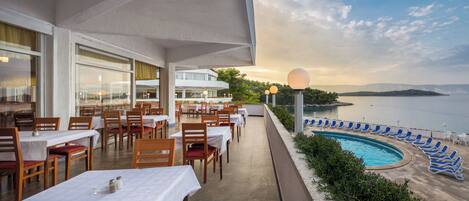 A restaurant with outdoor seating overlooking a pool and a lake.