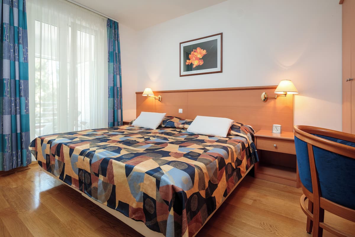 Una camera d'albergo con un letto grande, due comodini con lampade, una testiera in legno e un quadro incorniciato appeso al muro.