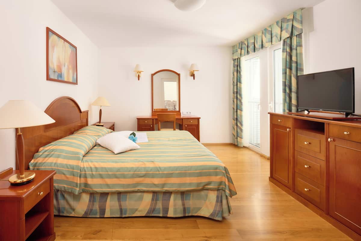 Una camera d'albergo con un letto, una scrivania, una televisione e una finestra con tende.