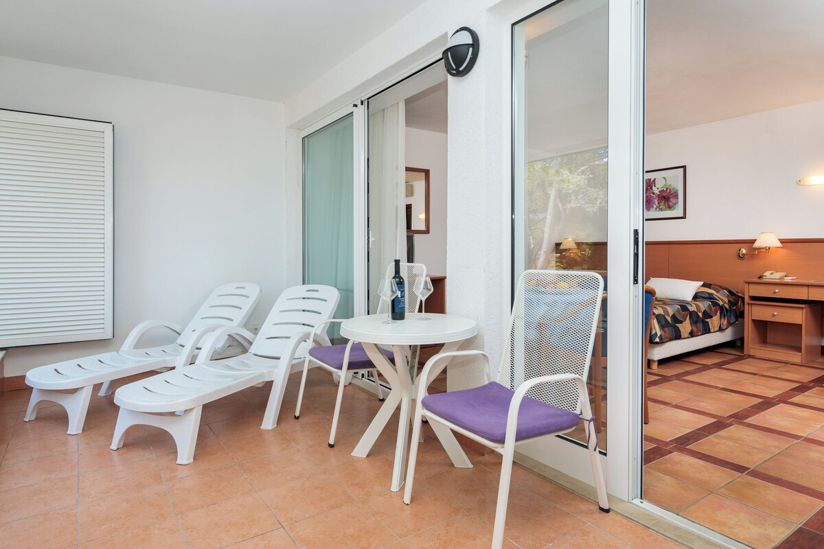 A balcony with white lounge chairs, a small table, and a chair with a purple cushion.