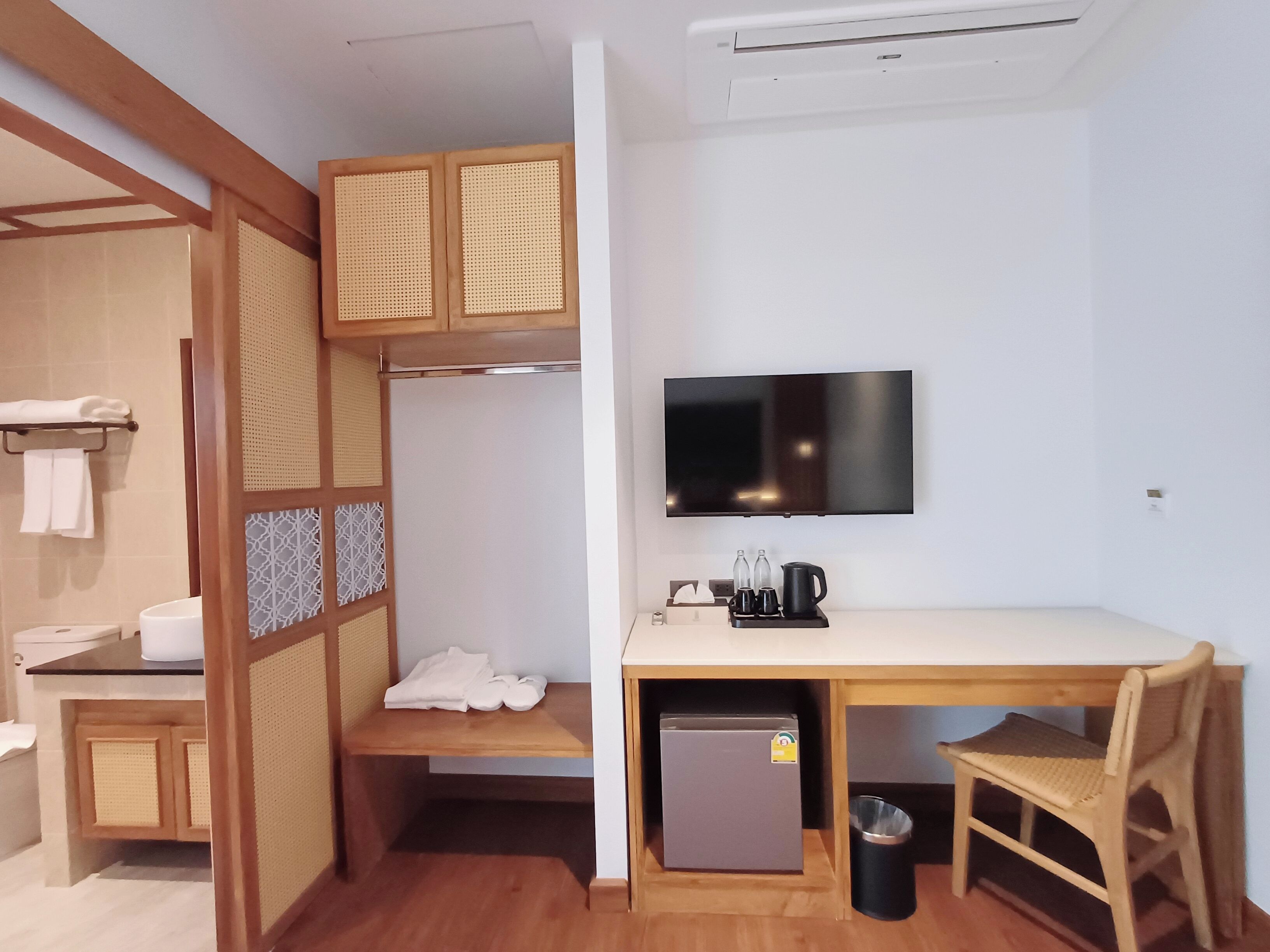 Habitación de hotel compacta con un escritorio de madera, televisor, refrigerador pequeño y un cubo de basura.
