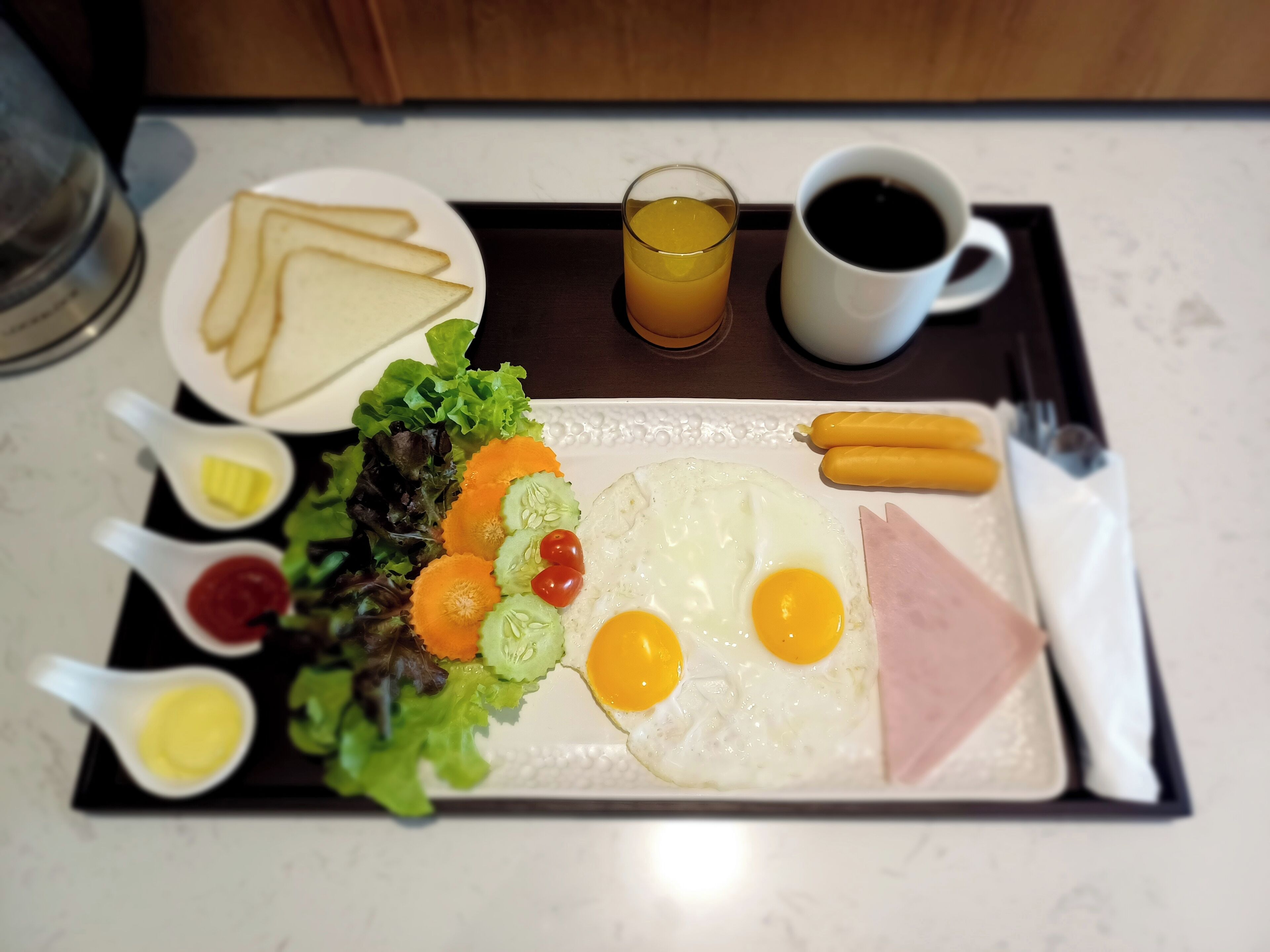 Ein Frühstücksbrett mit Eiern, Schinken, Würstchen, Toast, einem Salat und Getränken.