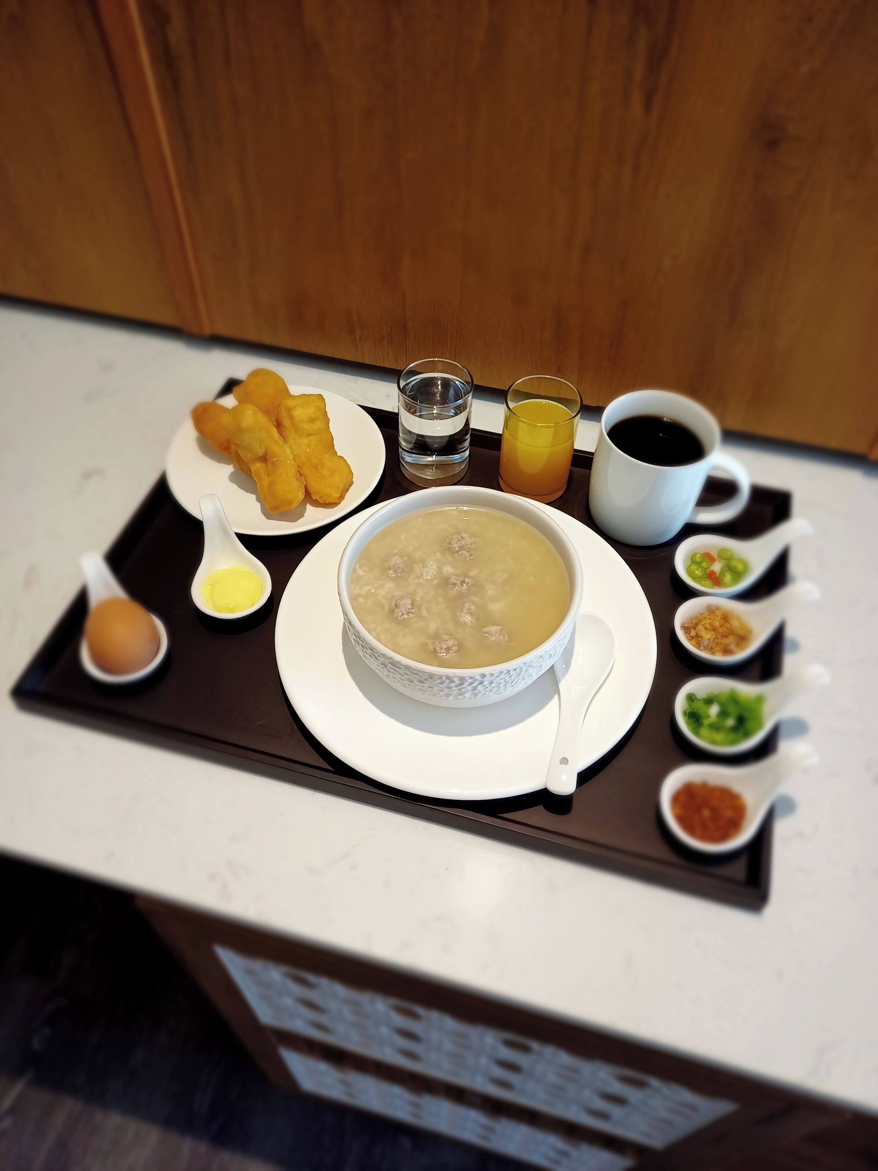 A breakfast tray with a bowl of soup, fried items, a glass of orange juice, a cup of coffee, and several condiments.