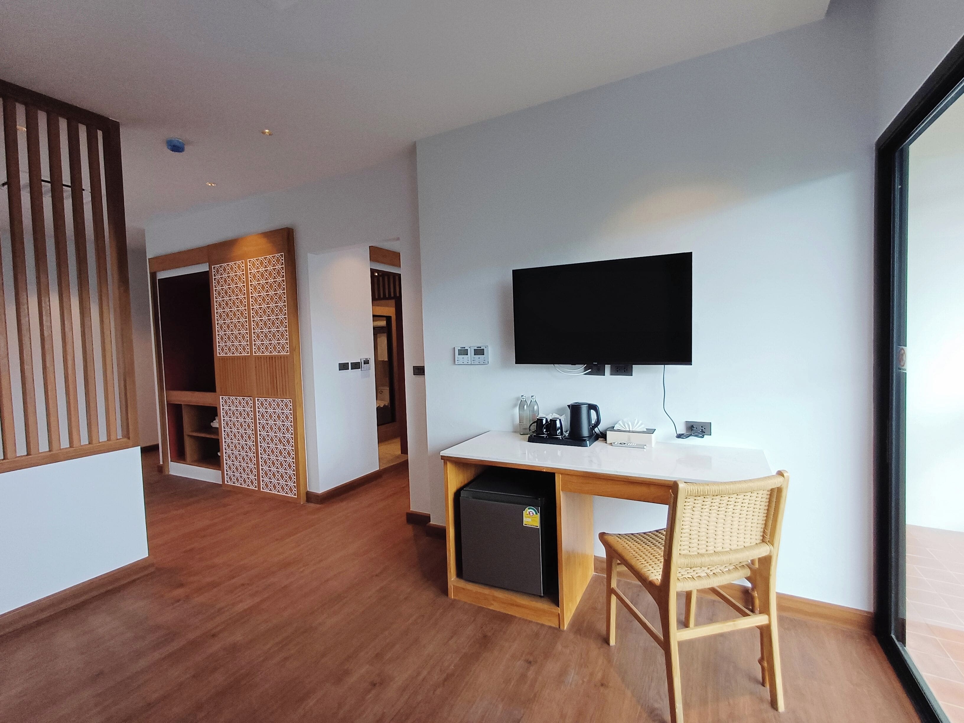 Een moderne kamer met een houten bureau, een aan de muur bevestigde televisie en een kleine koelkast.