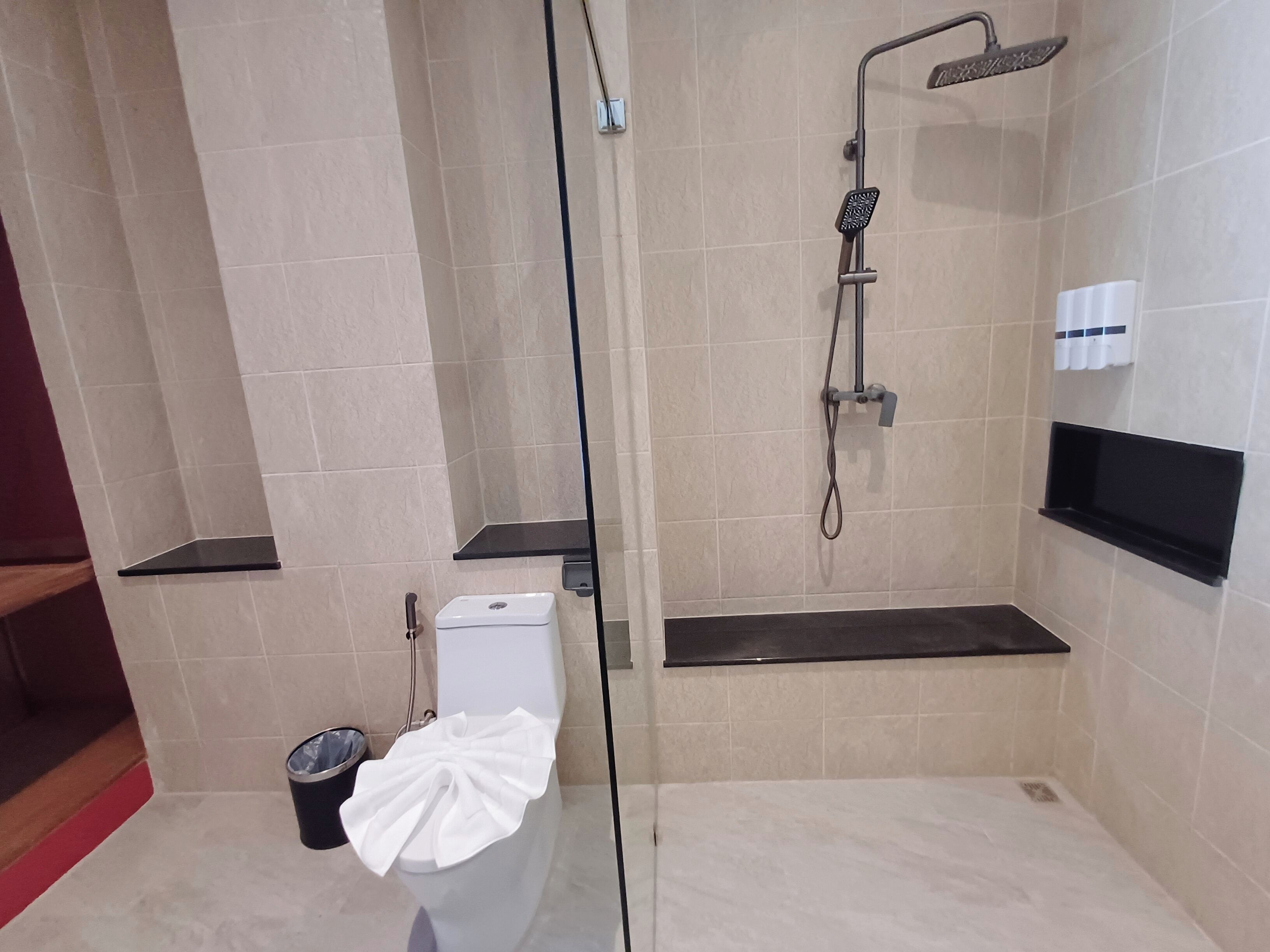 A modern bathroom with a glass-enclosed shower, a toilet, and a small trash bin.