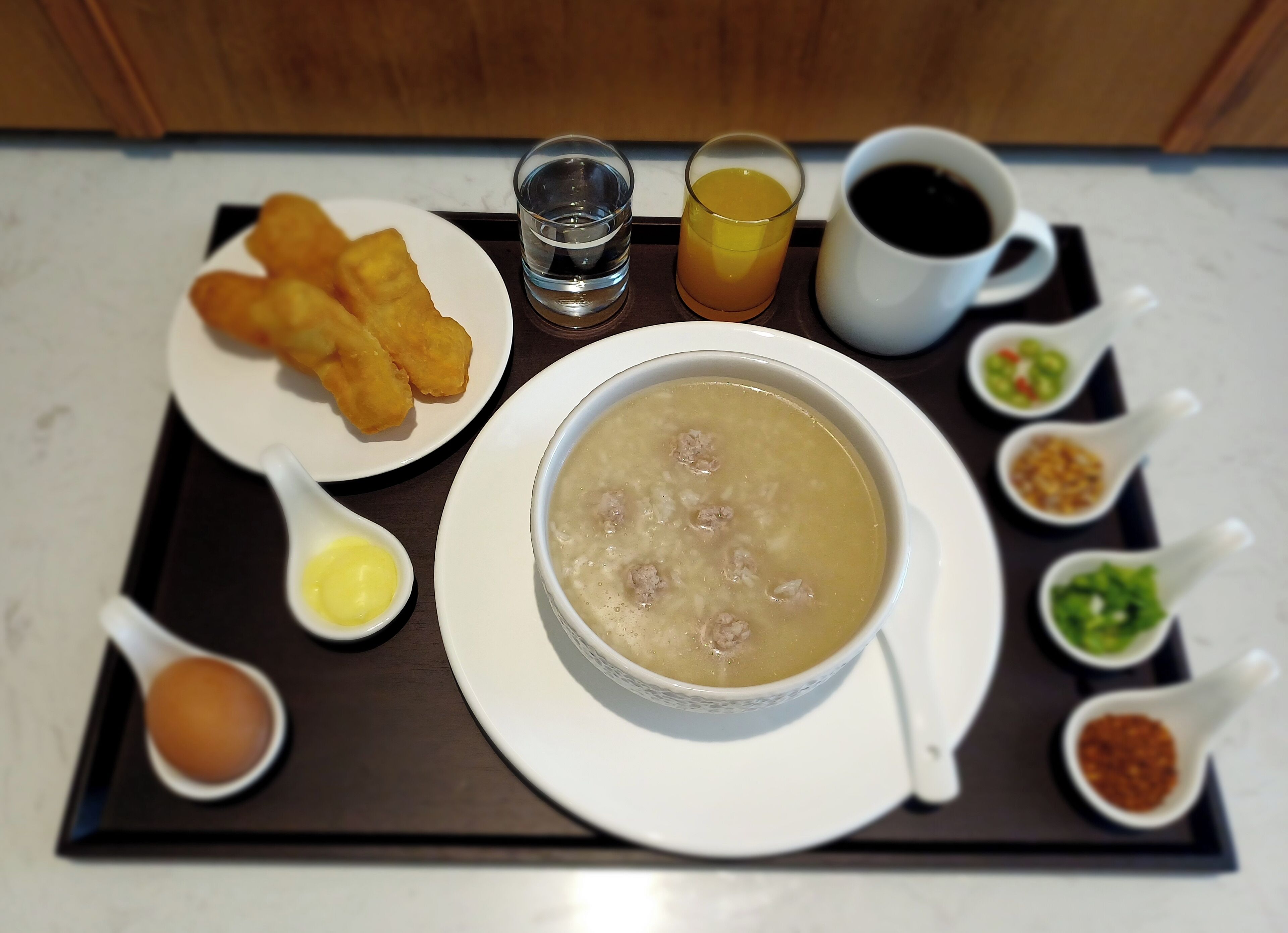 A tray with a bowl of soup, fried items, a glass of orange juice, a cup of coffee, and small bowls of condiments.