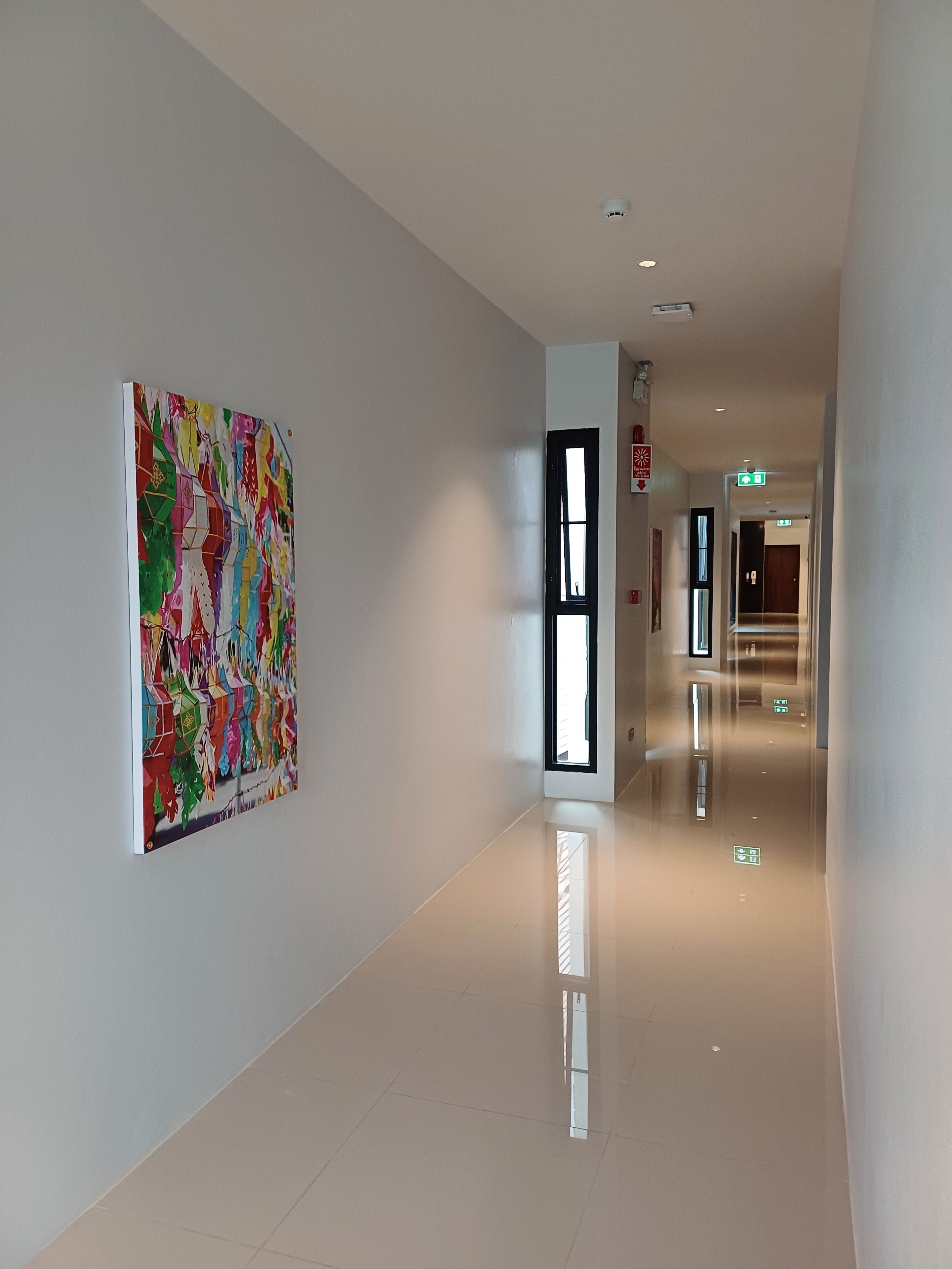 A hallway with a modern design, featuring a colorful abstract painting on the left wall, a door with a window on the right, and a clean, reflective floor.
