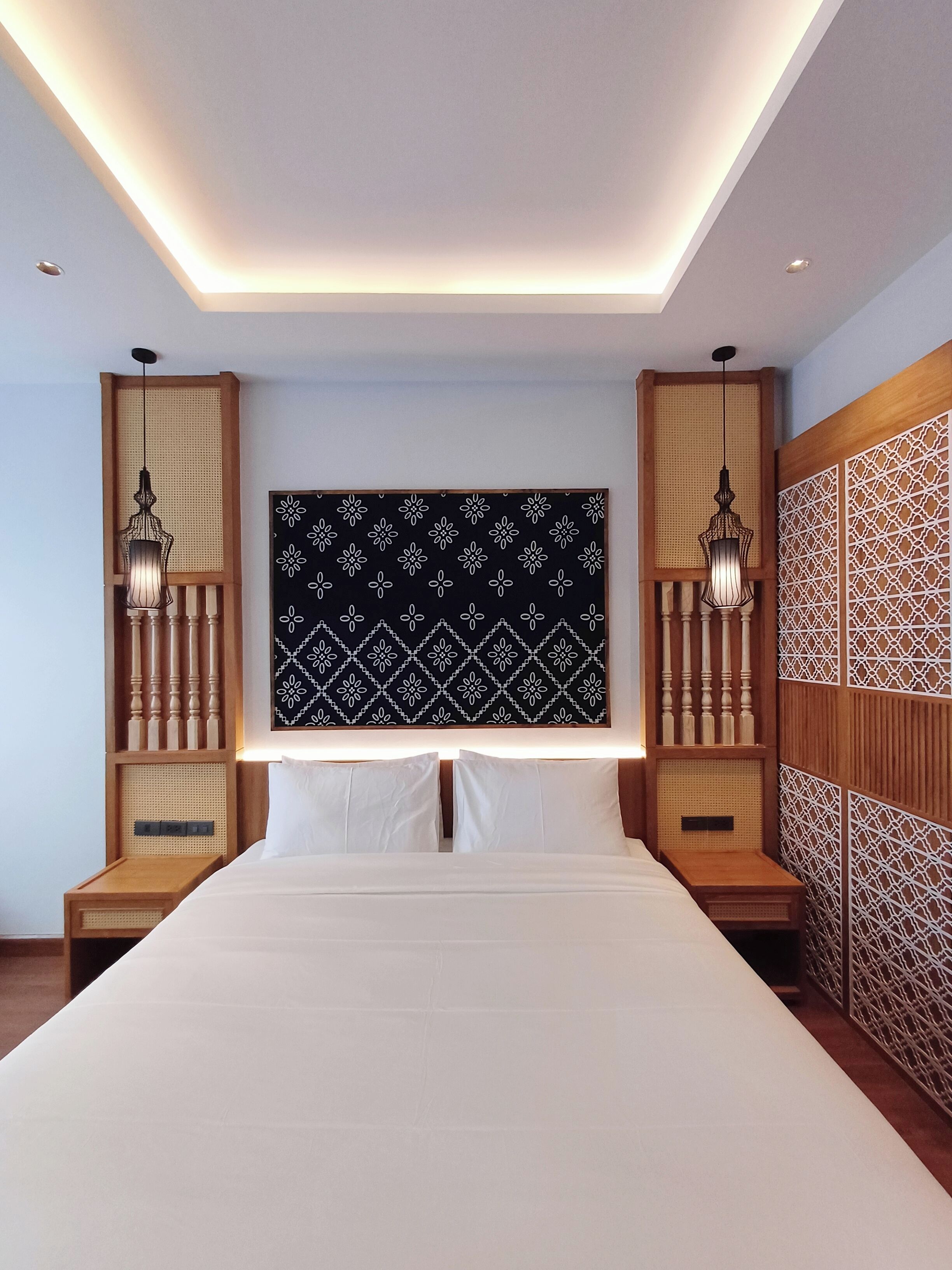 Une chambre d’hôtel moderne avec un grand lit, deux tables de chevet, une tête de lit à motifs et deux lampes fixées au mur.