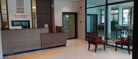 Uma área de recepção de hotel com balcão, porta de vidro que dá para a sala de jantar e alarme de incêndio visível.