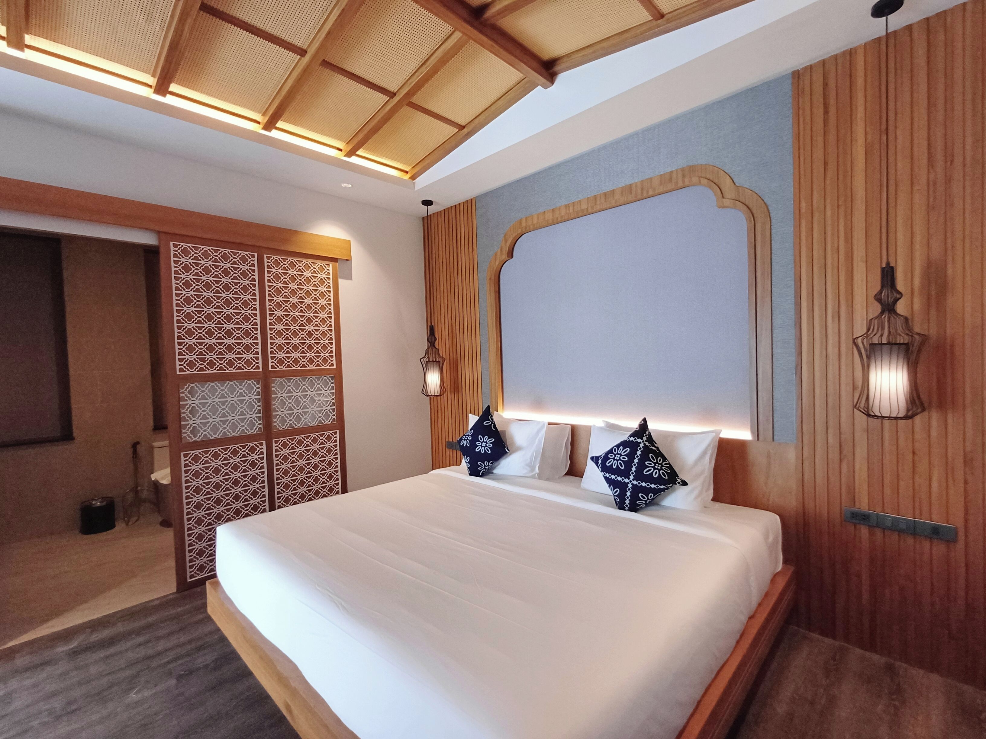 Una habitación de hotel moderna con una cama grande, paneles de madera y un techo decorativo.