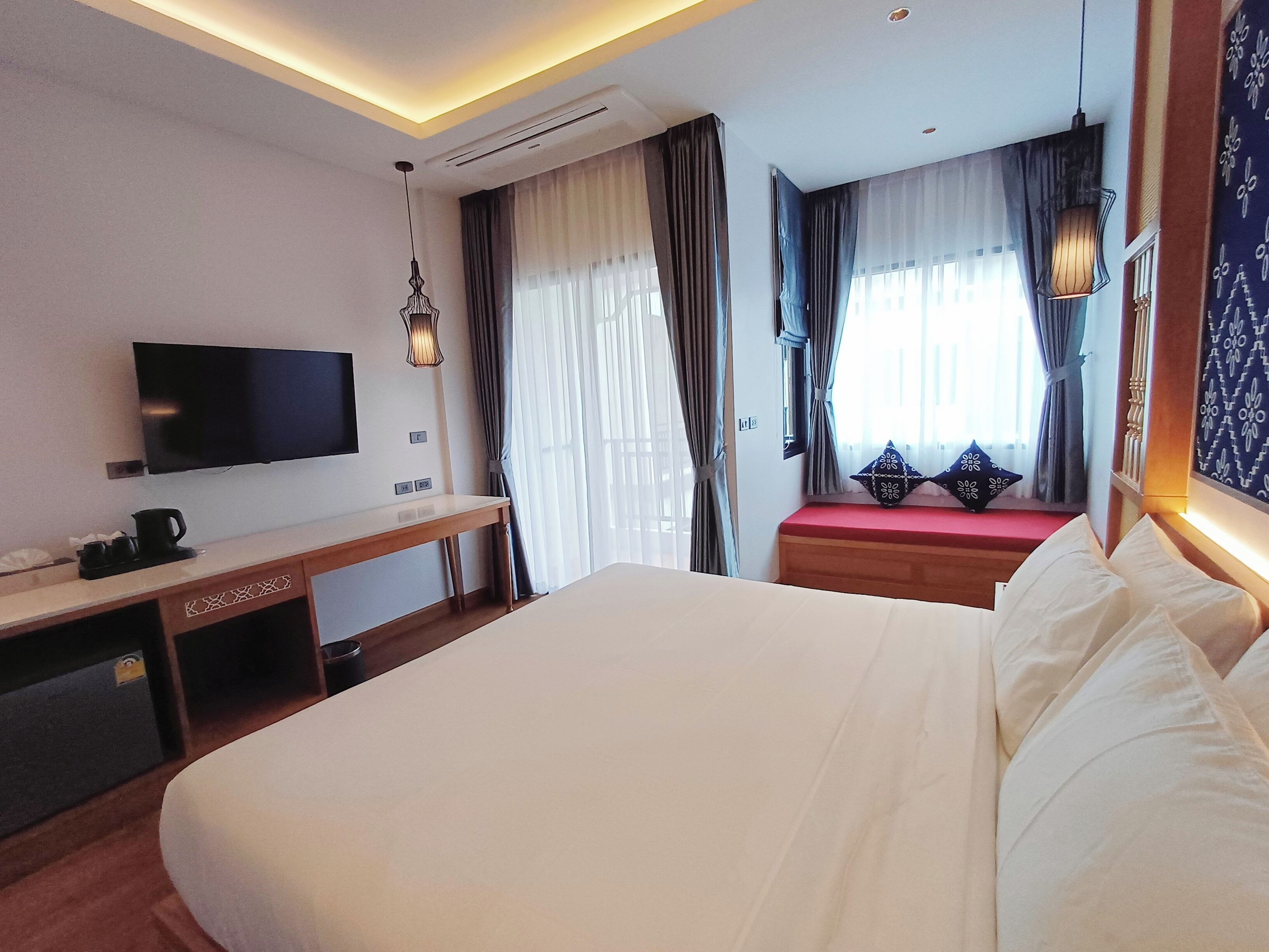 Ein Hotelzimmer mit einem großen Bett, einem Schreibtisch, einem Flachbildfernseher, einer Kaffeemaschine und einem Vorhangfenster.