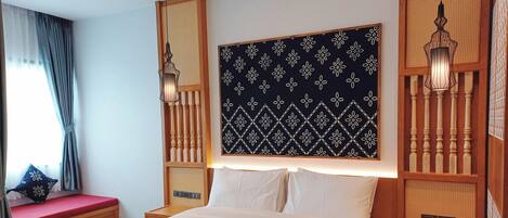 A hotel room with a large bed, a bedside table, a nightstand, a wall-mounted lamp, and a window with curtains.