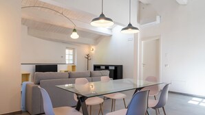 Un espace de repas moderne avec une table en verre et six chaises, un canapé gris et des luminaires suspendus.