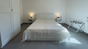 Une chambre à coucher au style minimaliste, avec un grand lit, deux tables de chevet avec des lampes, une armoire et un étendoir.