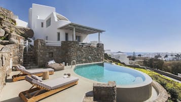 A modern villa with a swimming pool, stone walls, and lounge chairs.
