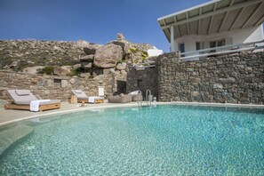 A clear swimming pool with lounge chairs and a stone wall. - Breathtaking 6 Bed in Platis Gialos (Platis Gialos)