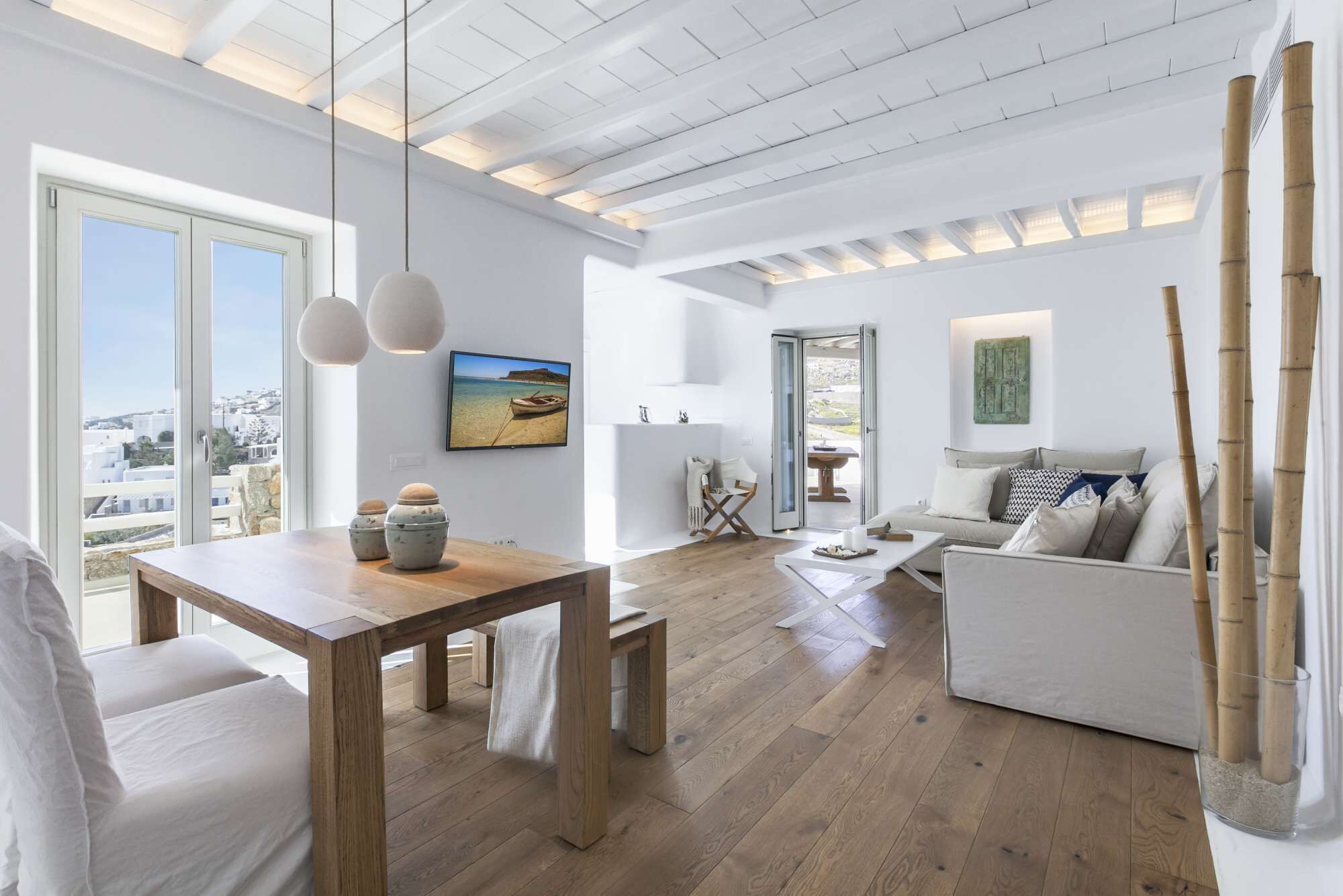 A spacious living room with a wooden dining table, a sofa, and a view of the city through large windows.