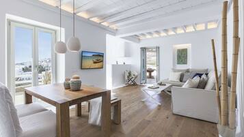 A spacious living room with a wooden dining table, a sofa, and a view of the city through large windows.