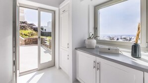 Une cuisine moderne avec des meubles blancs, un plan de travail en marbre et une vue sur la mer grâce à une grande fenêtre.