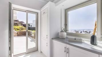 A modern kitchen with white cabinetry, a marble countertop, and a view of the sea through a large window.
