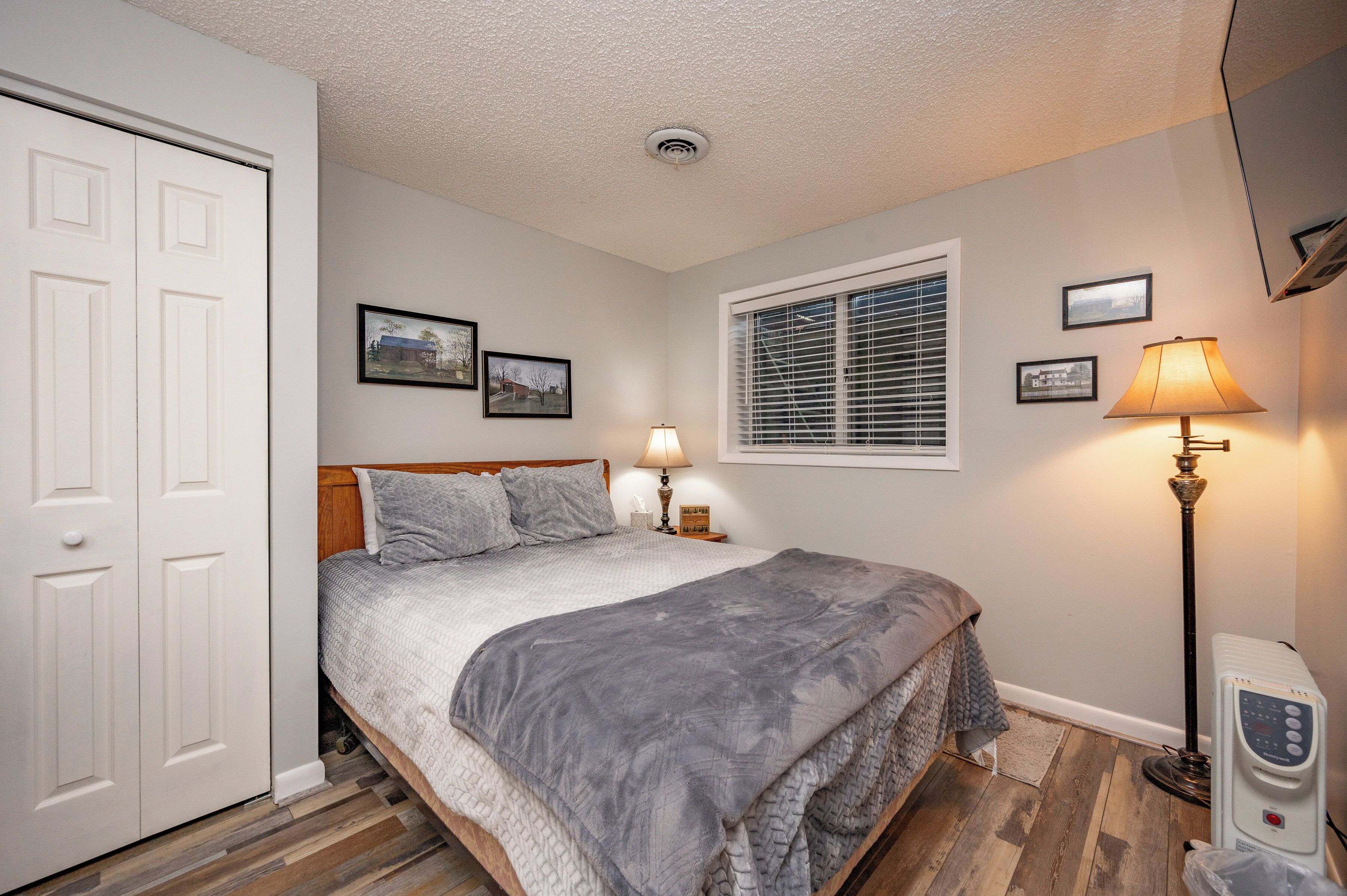 A bedroom with a bed, bedside lamps, a heater, a window with blinds, and a door.