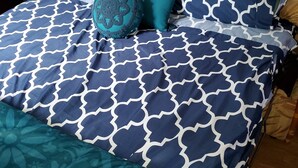 Een bed met een beddegoed in blauw-wit patroon, een teal kussen en een houten hoofdbord.