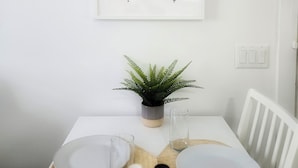A dining area with a white table, two framed turtle silhouettes, a potted plant, and a white chair.