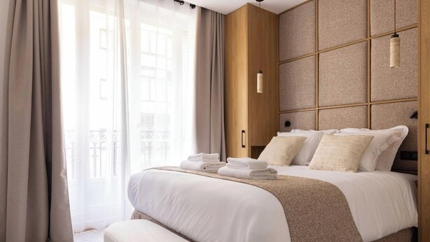 A modern hotel room with a large bed, a wooden headboard, and a view of the city through large windows. - A BLEND OF MINIMALIST ELEGANCE, PARISIAN FLAIR NEAR RUE MOUFFETARD-LATIN QUARTER (Paris)