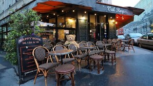 An outdoor cafe with wicker chairs and tables, a teddy bear decoration, and a menu board advertising happy hour. - A BLEND OF MINIMALIST ELEGANCE, PARISIAN FLAIR NEAR RUE MOUFFETARD-LATIN QUARTER (Paris)