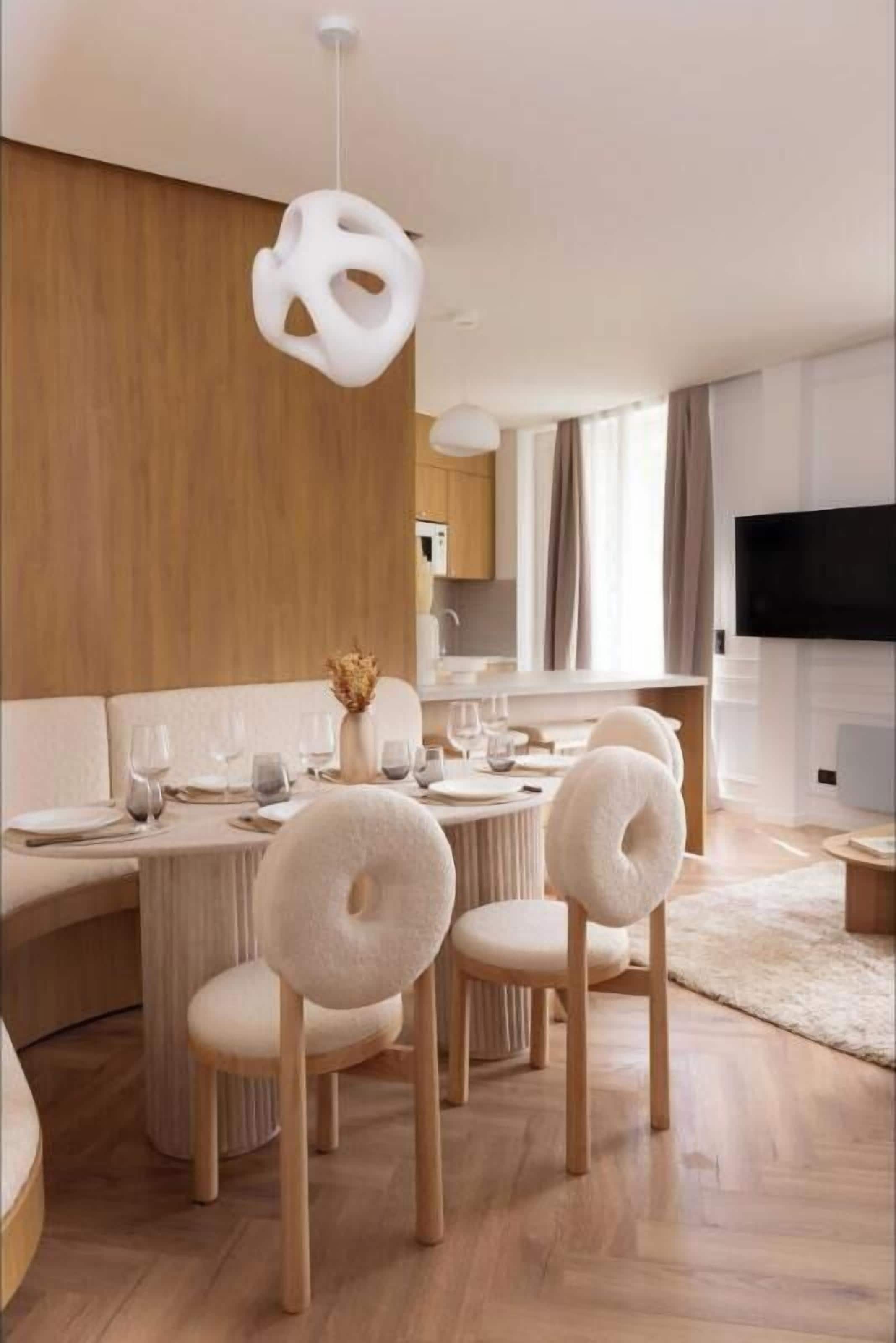 A modern dining area with a round table, white chairs, and a unique pendant light.