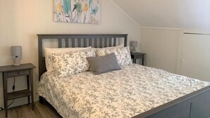 A bedroom with a bed, two bedside tables, a nightstand, a wall-mounted painting, and a wardrobe.