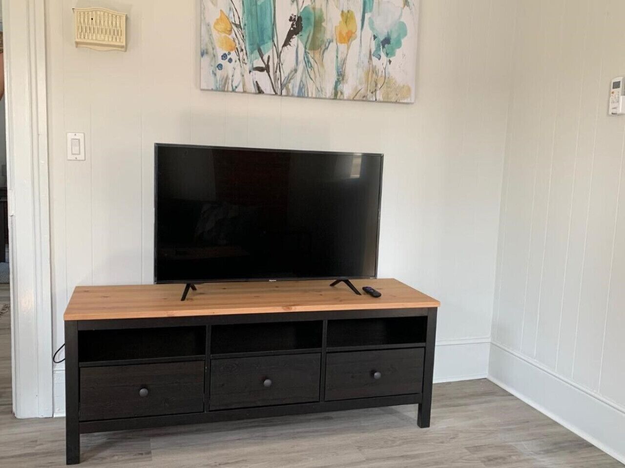 A wooden TV stand with a flat-screen TV, three drawers, and a remote control on top.