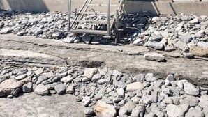 Et hus med en betontrappe, der fører op til en veranda, omgivet af sten og vegetation.