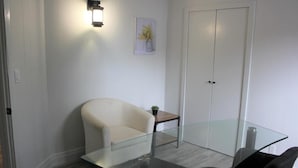 A modern office space with a glass table, a white armchair, a small wooden side table, and a wall-mounted light fixture. - Two-Bedroom Wellington Apartment (Prince Edward)