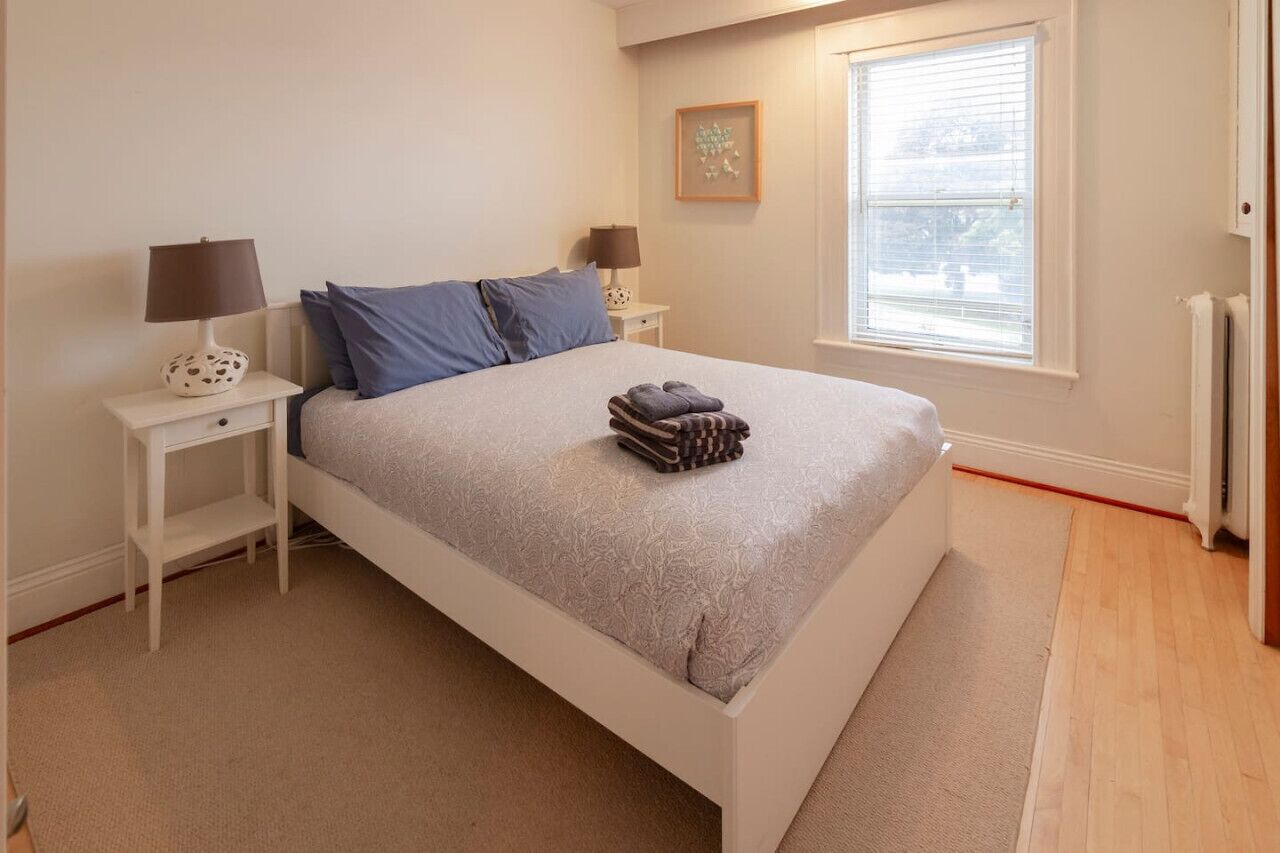 A bedroom with a bed, two bedside tables, a window, and a radiator.